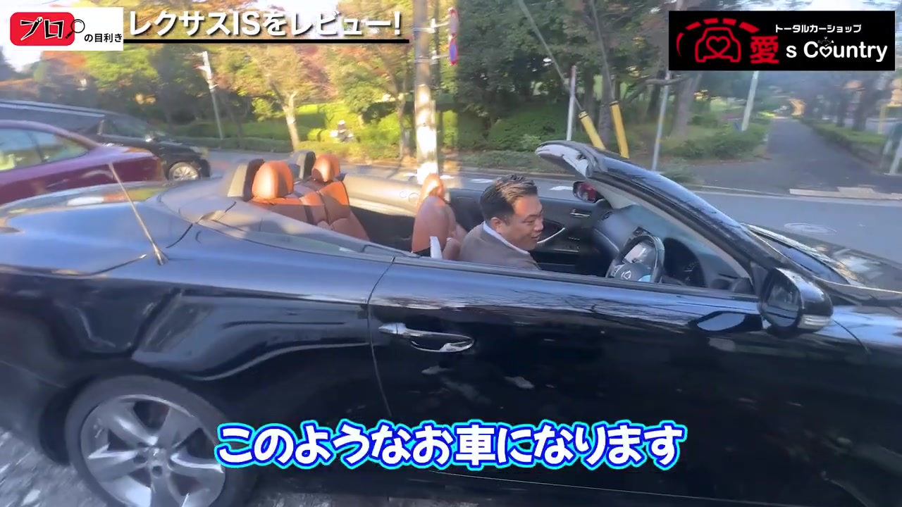 屋根を格納したレクサスISのオープンモデル(黒)を運転席から見せる社長