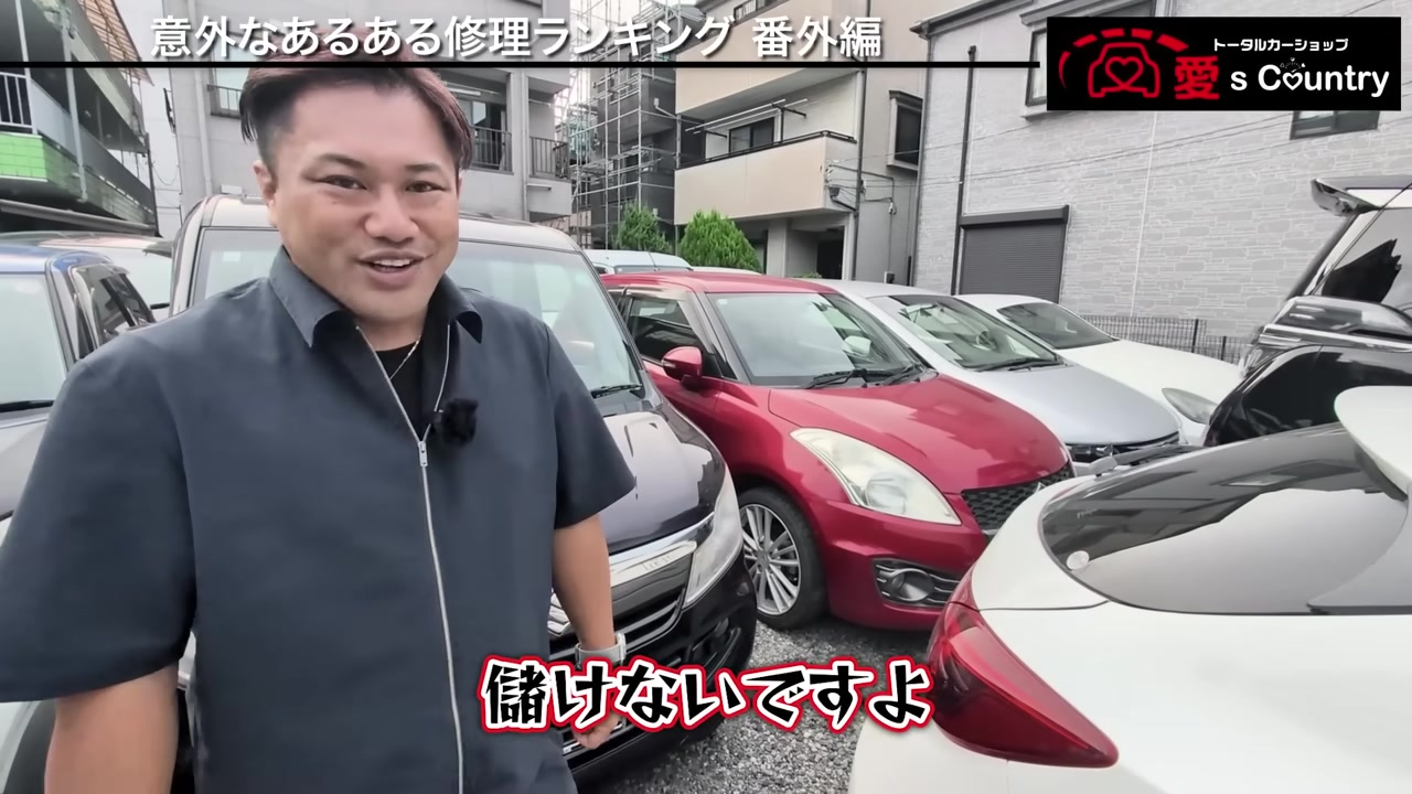在庫車が並ぶ販売店の駐車場に立つ社長