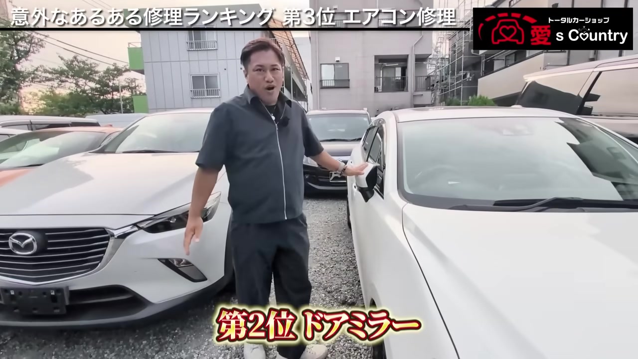 白いマツダ車のドアミラーに手を添えて説明する社長